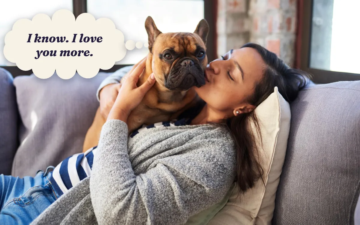 Woman kissing her French bulldog at home, thinking "I know. I love you more."